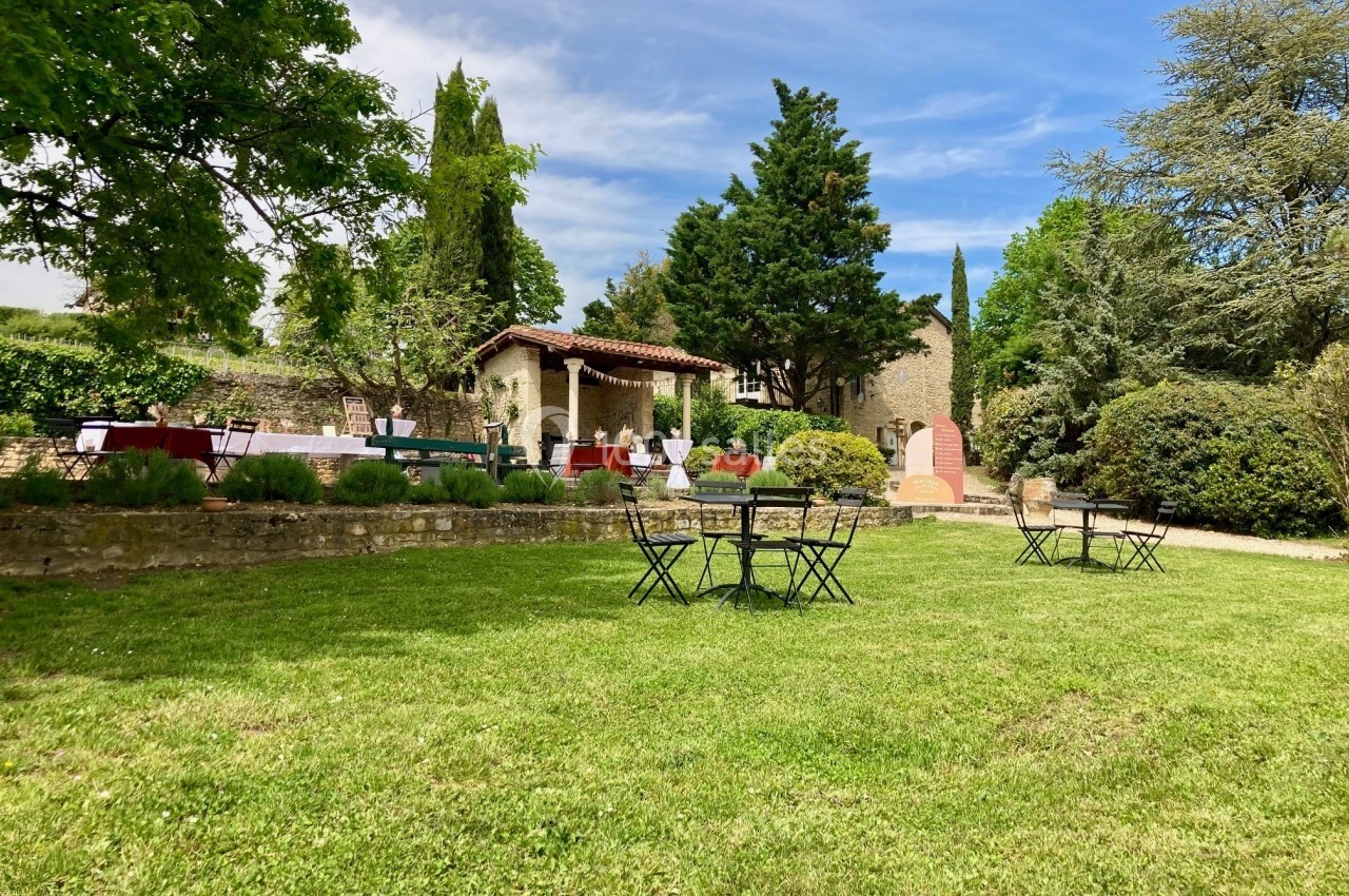 Jardin verdoyant avec tables et chaises en métal noir, entouré de végétation et de bâtiments en pierre.
