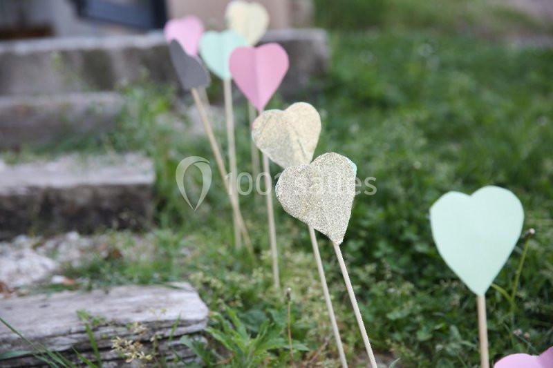 Cœurs en papier colorés fixés sur des tiges en bois, plantés dans l'herbe près de marches en pierre.
