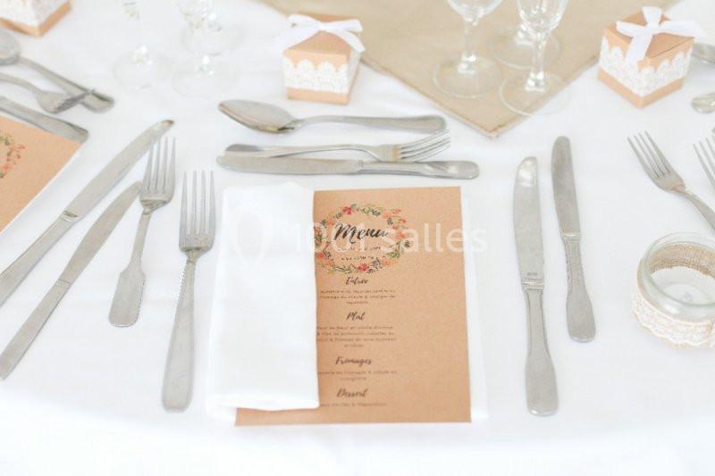 Table dressée avec des couverts en métal, un menu imprimé, des verres et des boîtes cadeaux décoratives.