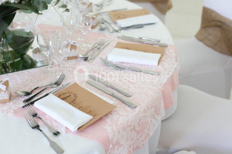 Table dressée avec nappe rose, couverts, serviettes blanches, menus et centre de table floral.