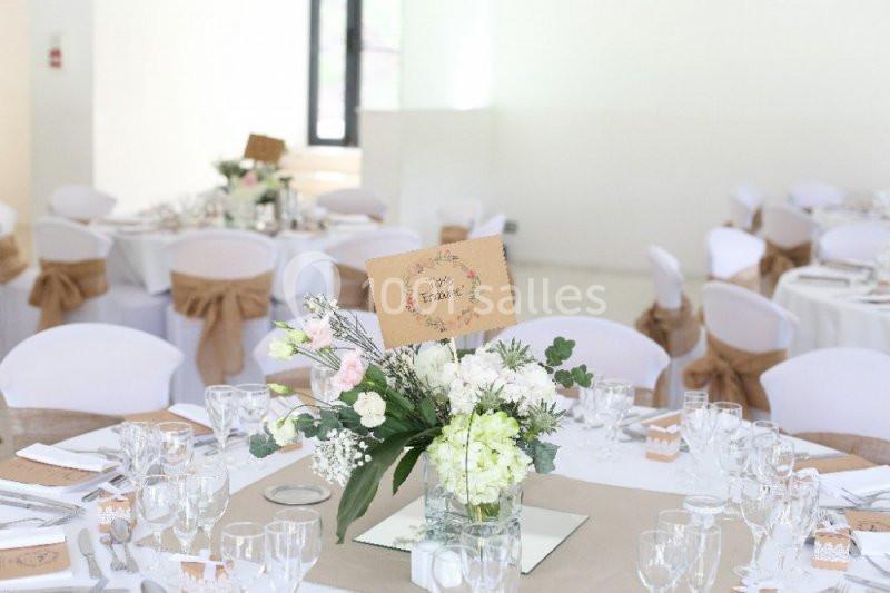 Salle de réception lumineuse avec des tables décorées de nappes blanches, centres de table fleuris et marque-places.
