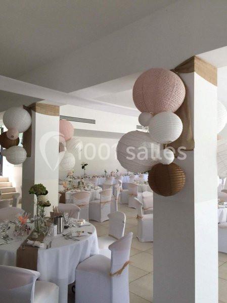 Salle de réception décorée avec des lanternes suspendues et des tables dressées pour un événement festif.