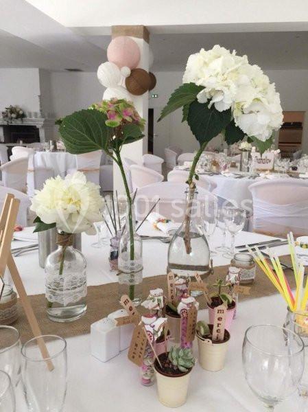 Décoration de table avec fleurs blanches et roses dans des vases en verre, petits pots de plantes et accessoires de mariage.