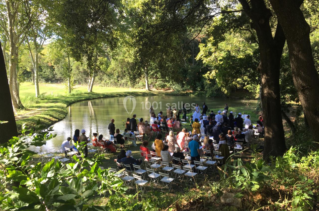 Un groupe de personnes assises et debout près d'un étang entouré d'arbres lors d'un événement en plein air.