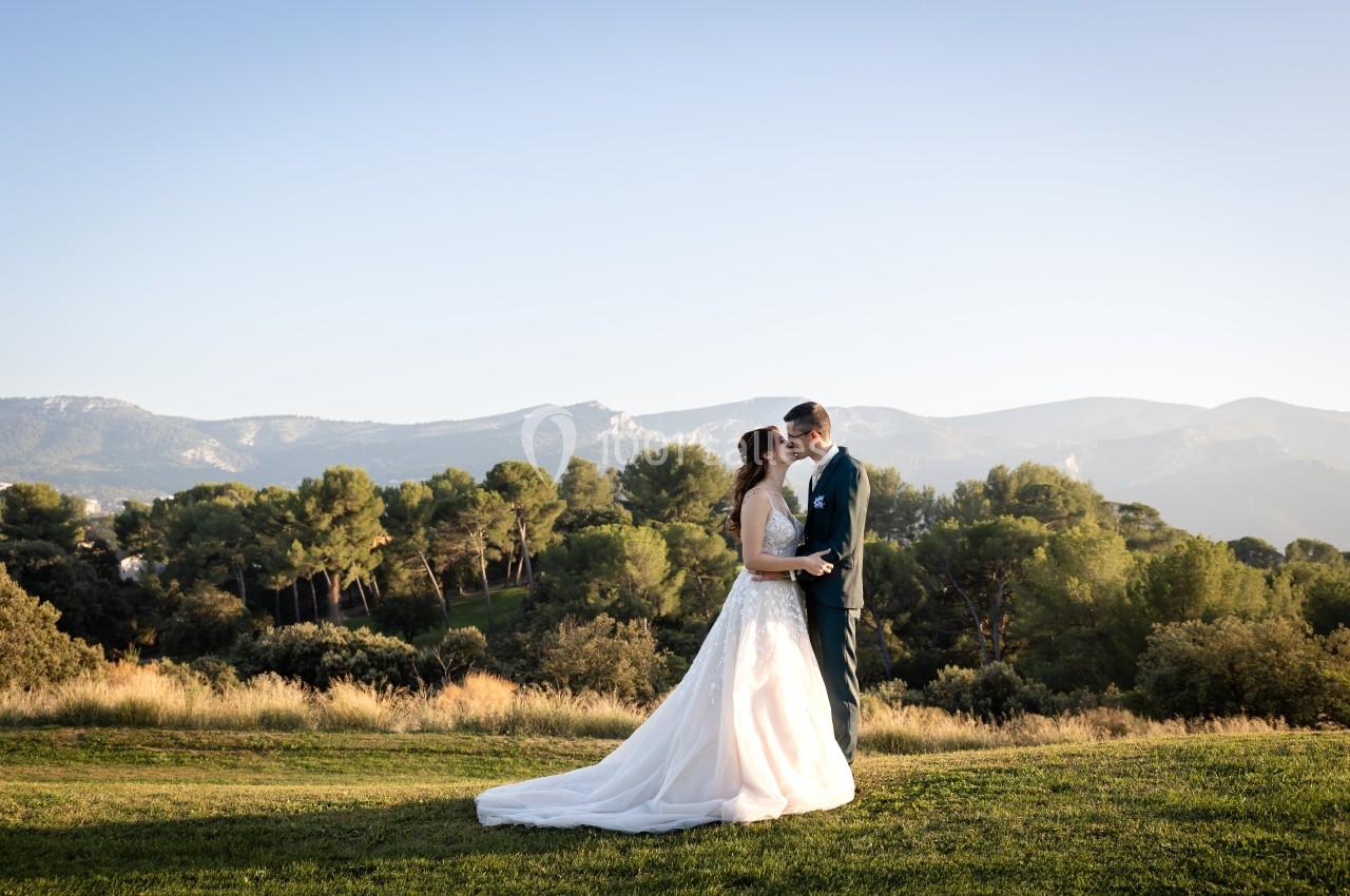 Un couple en tenue de mariage se tient dans un paysage naturel avec des collines et des arbres en arrière-plan.