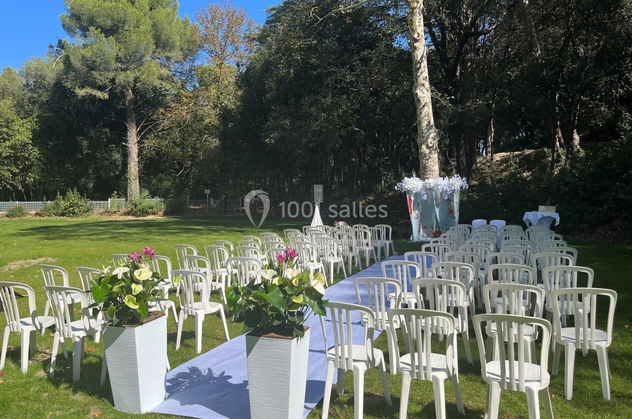 Chaises blanches disposées en rangées sur une pelouse, avec une allée centrale décorée pour une cérémonie en extérieur.
