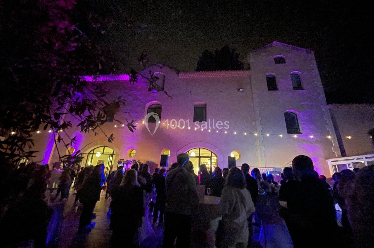 Façade d'un bâtiment éclairé par des lumières colorées, avec une foule rassemblée en soirée.