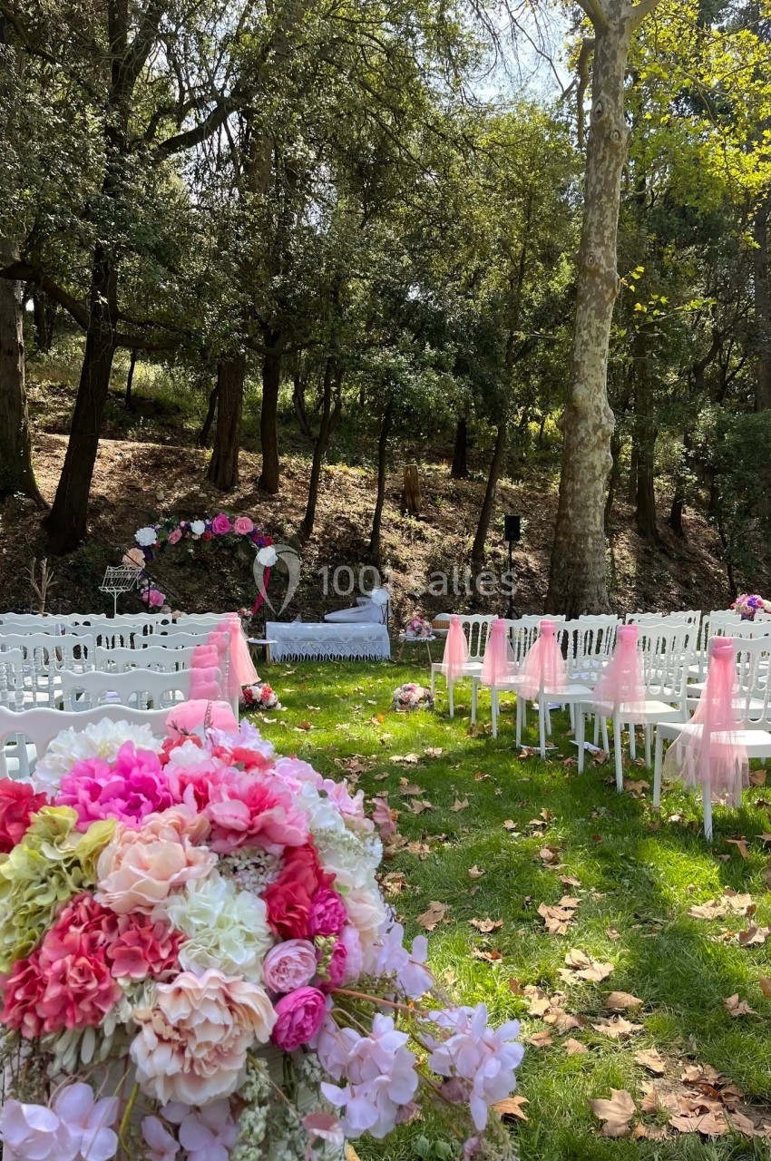 Chaises blanches alignées sur une pelouse avec des décorations florales roses, prêtes pour une cérémonie en plein air.
