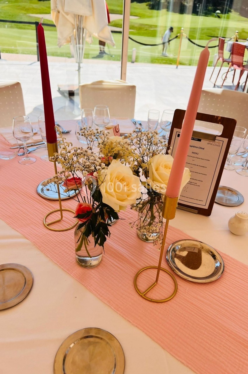 Table décorée avec des chandeliers, des roses blanches et roses, et un menu sur fond de nappe rose.