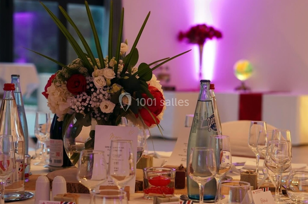 Table de réception élégamment dressée avec des fleurs, verres, bouteilles d'eau et lumière d'ambiance violette en arrière…