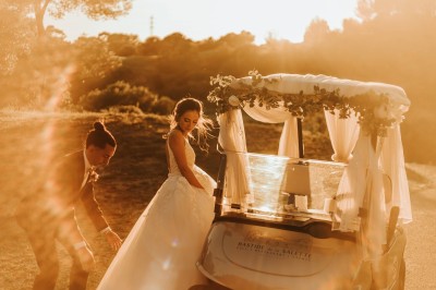 Une mariée en robe blanche danse en extérieur, tenant des rubans entourée d'invités en tenue de soirée.