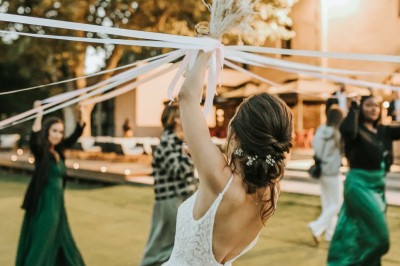 Une mariée en robe blanche danse en extérieur, tenant des rubans entourée d'invités en tenue de soirée.