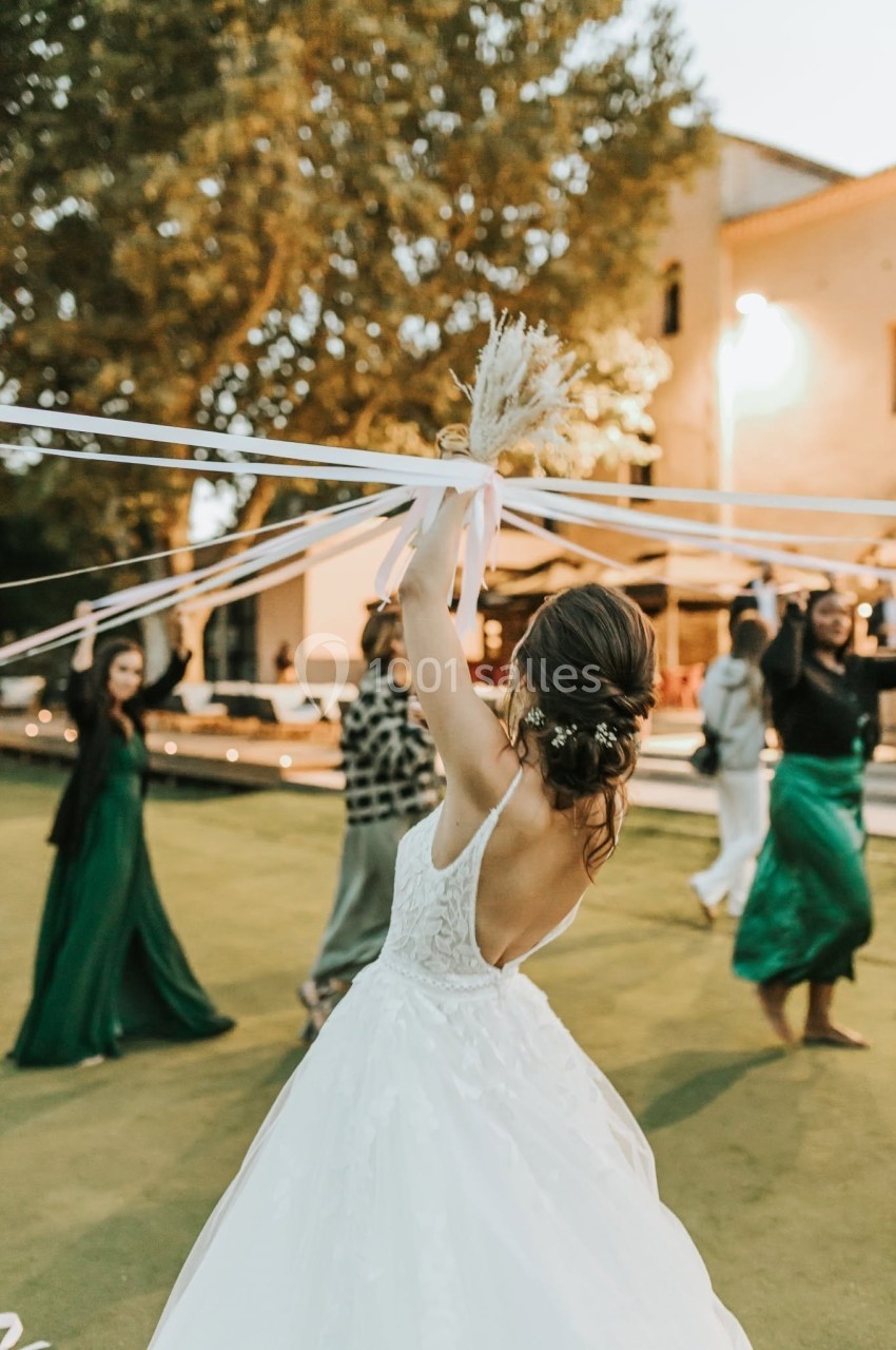 Une mariée en robe blanche danse en extérieur, tenant des rubans entourée d'invités en tenue de soirée.