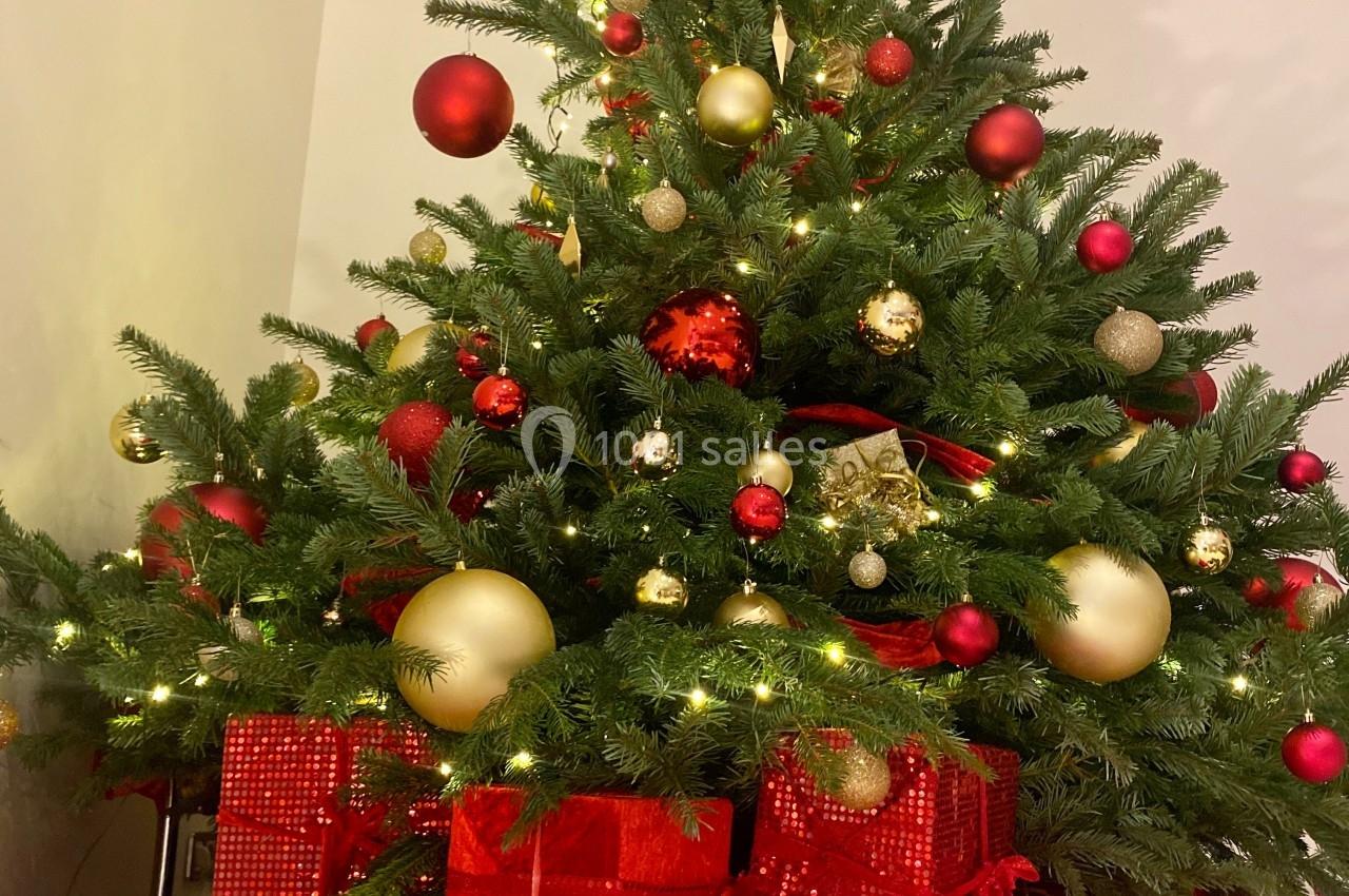 Sapin de Noël décoré avec des boules rouges et dorées, entouré de cadeaux emballés dans du papier coloré.