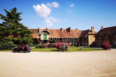 Un groupe de femmes, dont une en robe blanche, marche sur une pelouse devant un bâtiment en pierre et bois.
