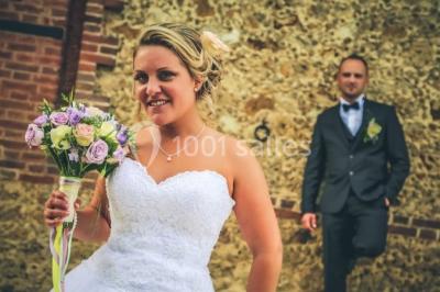 Un groupe de femmes, dont une en robe blanche, marche sur une pelouse devant un bâtiment en pierre et bois.