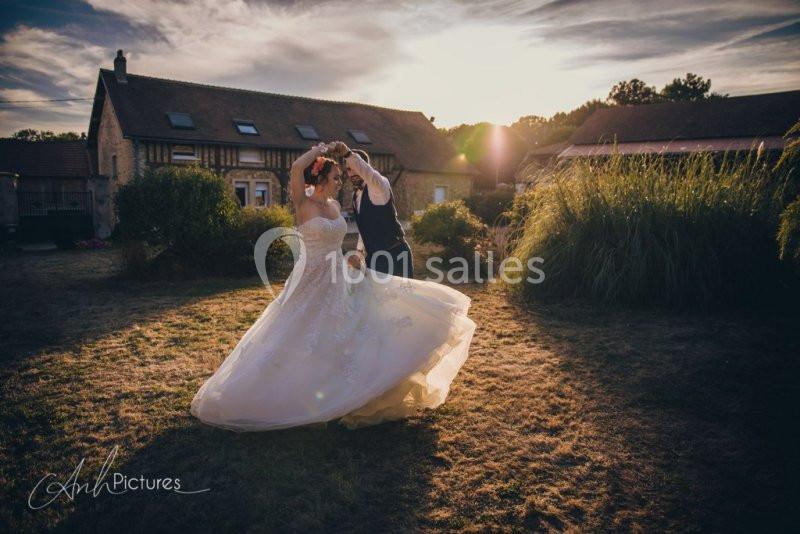 Un couple danse en tenue de mariage dans un jardin au coucher du soleil, devant des bâtiments en pierre.