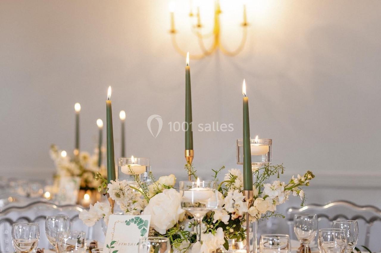 Table élégamment dressée avec chandeliers verts, fleurs blanches et décoration raffinée dans une ambiance lumineuse.