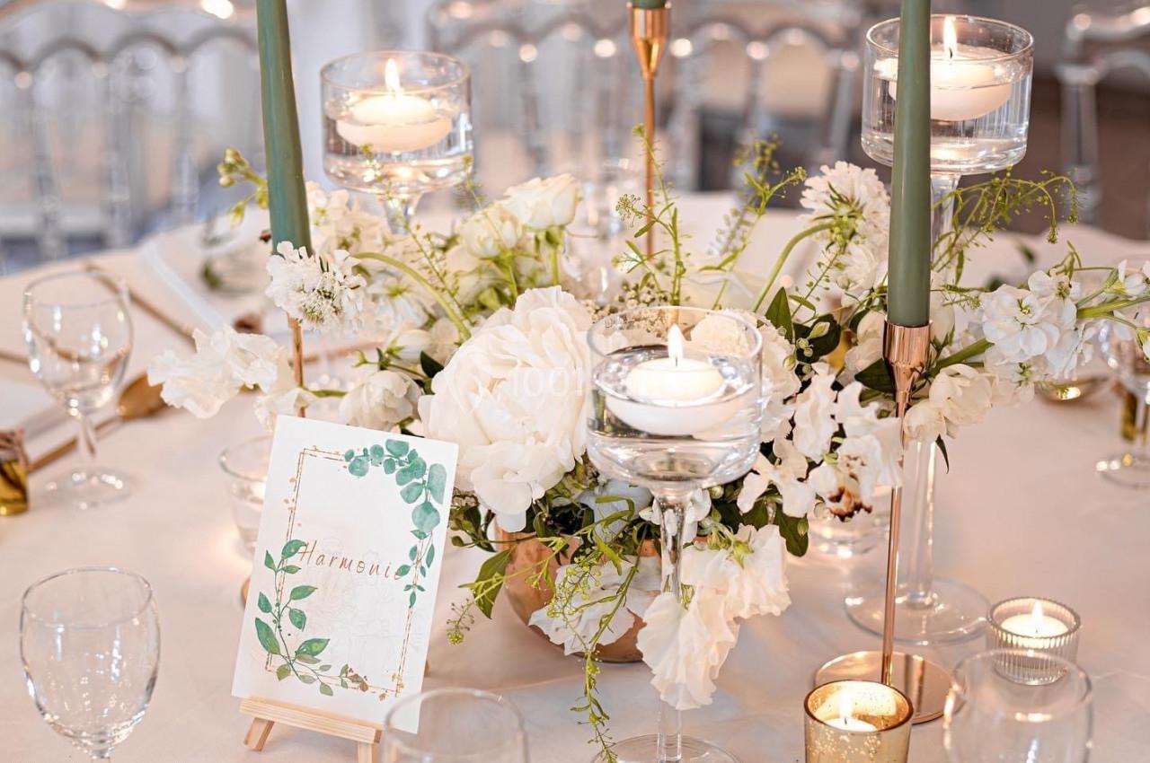 Table élégamment dressée avec bougies, fleurs blanches, verres et carte décorative sur un chevalet.