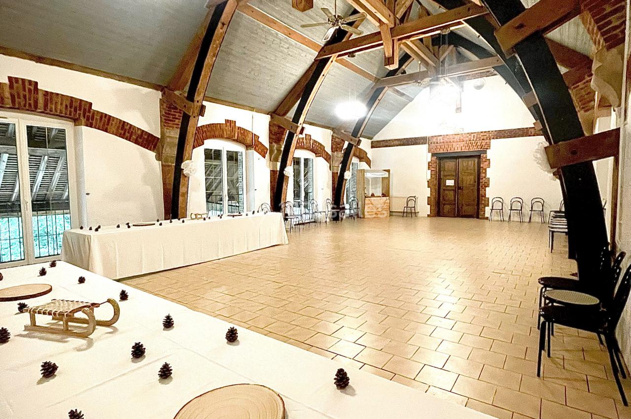 Salle spacieuse avec charpente en bois apparente, tables décorées de pommes de pin et grandes fenêtres donnant sur l…