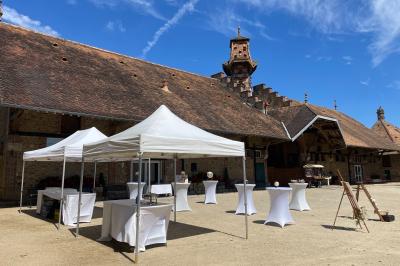 Un groupe de femmes, dont une en robe blanche, marche sur une pelouse devant un bâtiment en pierre et bois.