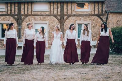 Un groupe de femmes, dont une en robe blanche, marche sur une pelouse devant un bâtiment en pierre et bois.