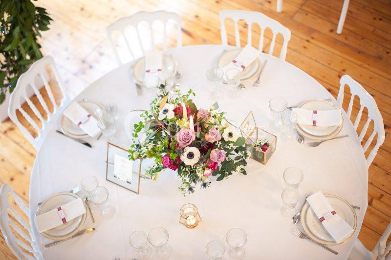 Table ronde décorée avec une nappe blanche, un centre de table floral coloré et des couverts élégamment disposés.