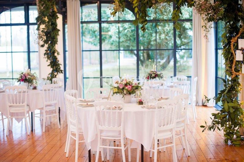 Salle décorée pour un événement avec des tables rondes, nappes blanches, chaises assorties et arrangements floraux.