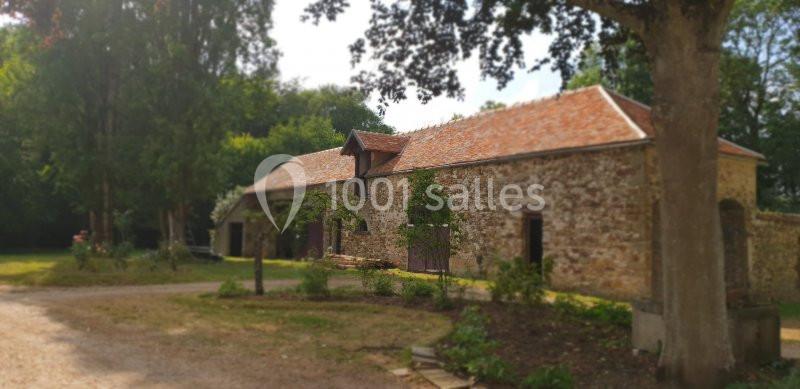 Bâtiment en pierre avec toit en tuiles rouges, entouré d'arbres et d'un espace extérieur verdoyant.