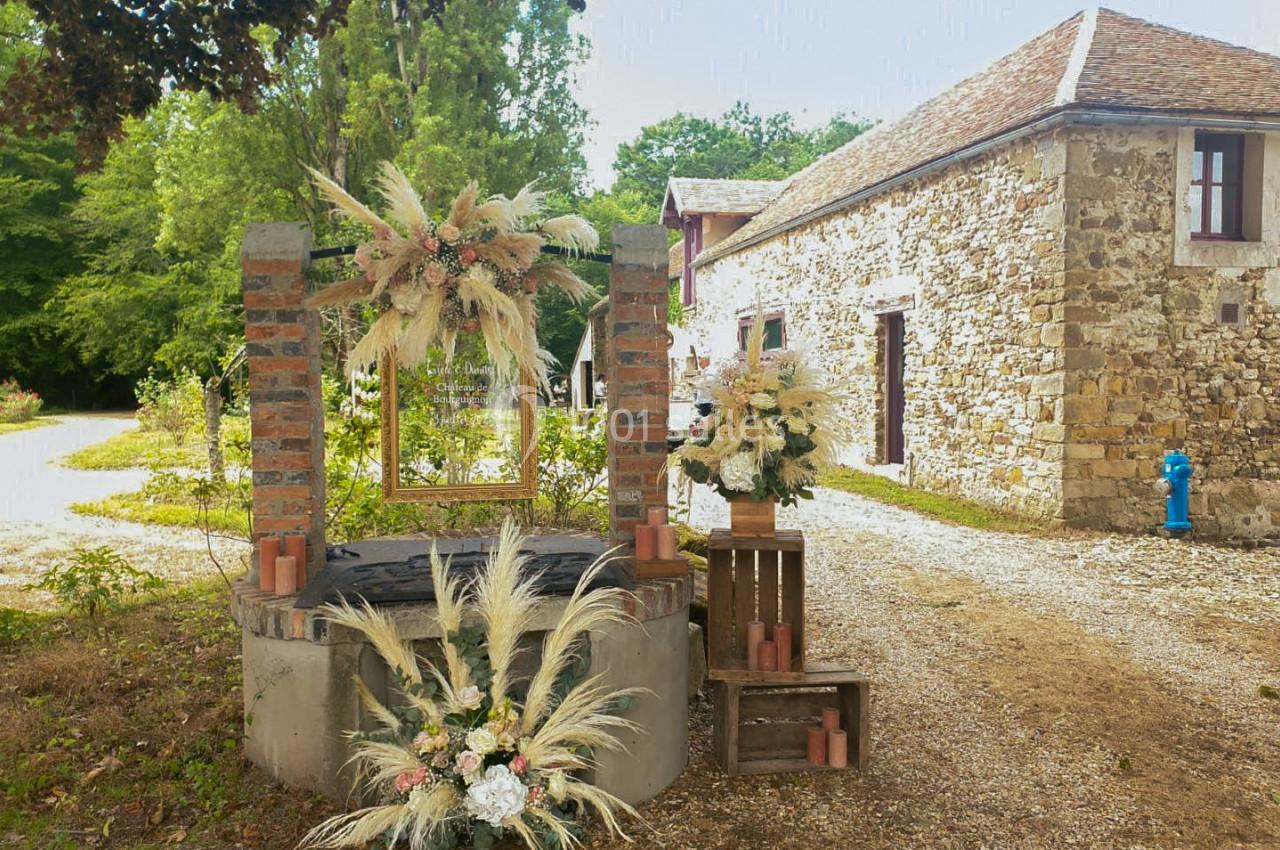 Décoration florale avec des herbes séchées et des fleurs autour d'un puits en pierre, près d'une maison en pierre.