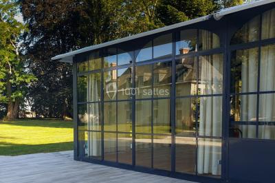 Vue nocturne d'une verrière illuminée par des lumières violettes, entourée d'arbres et d'un jardin.