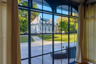 Vue nocturne d'une verrière illuminée par des lumières violettes, entourée d'arbres et d'un jardin.