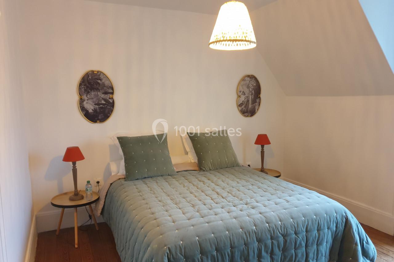 Chambre avec un lit double, couvre-lit bleu, deux tables de chevet avec lampes rouges et un lustre suspendu.