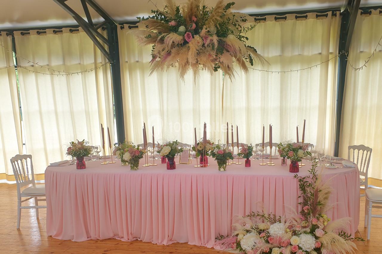 Table de réception décorée de fleurs, bougies et nappes roses, avec un grand arrangement floral suspendu.