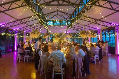 Vue nocturne d'une verrière illuminée par des lumières violettes, entourée d'arbres et d'un jardin.