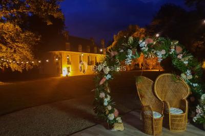 Vue nocturne d'une verrière illuminée par des lumières violettes, entourée d'arbres et d'un jardin.