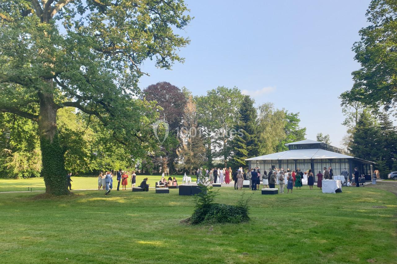 Groupe de personnes rassemblées près d'un bâtiment vitré dans un parc verdoyant par une journée ensoleillée.