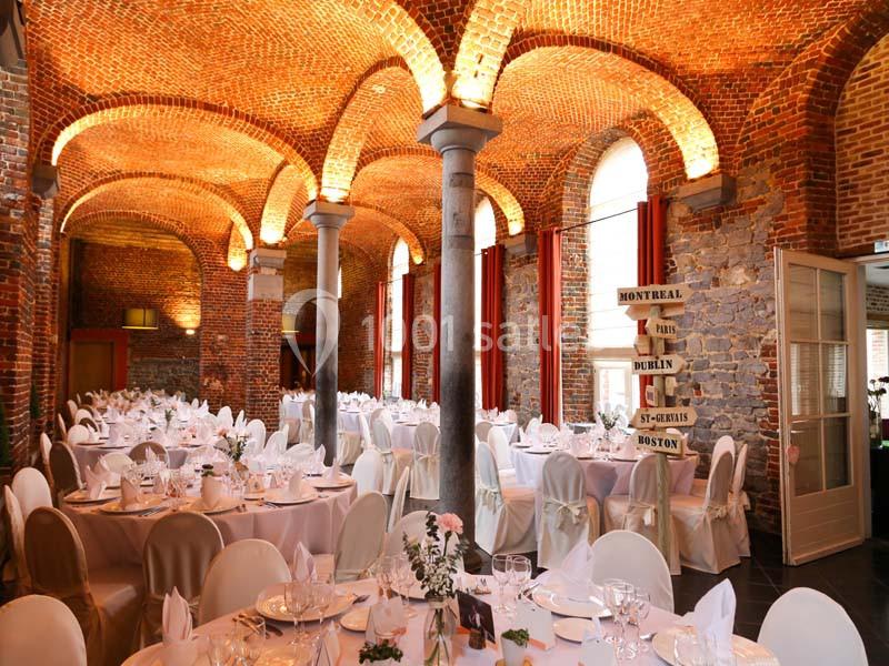 Salle de réception avec murs en briques, tables décorées pour un événement et panneaux directionnels en bois.