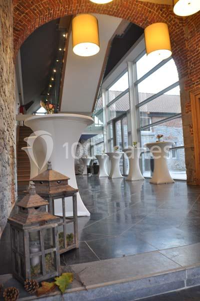 Intérieur lumineux avec murs en briques, tables hautes blanches et grandes fenêtres donnant sur une cour.