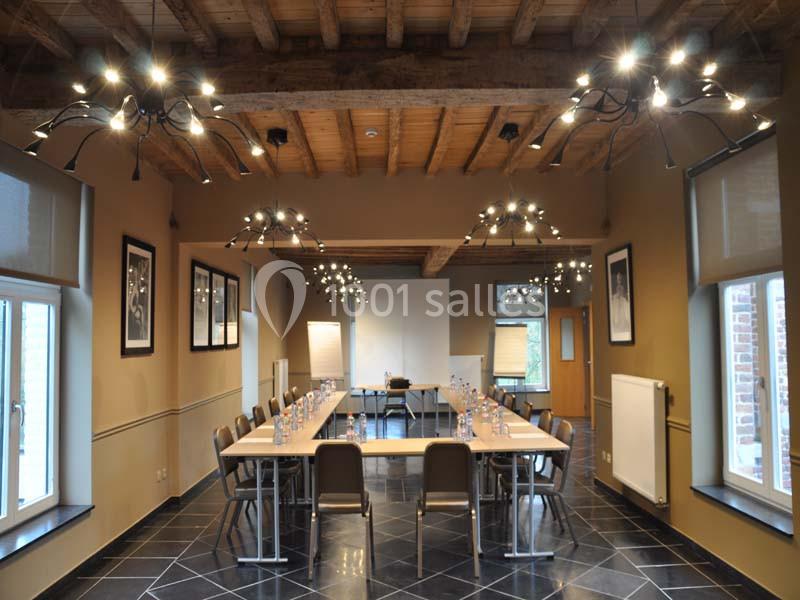 Salle de réunion lumineuse avec grande table rectangulaire, chaises, tableau blanc et poutres apparentes au plafond.