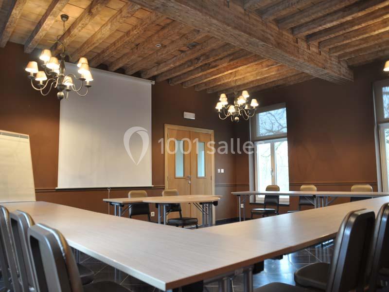 Salle de réunion avec tables disposées en U, chaises, écran de projection, tableau blanc et plafond en bois apparent.