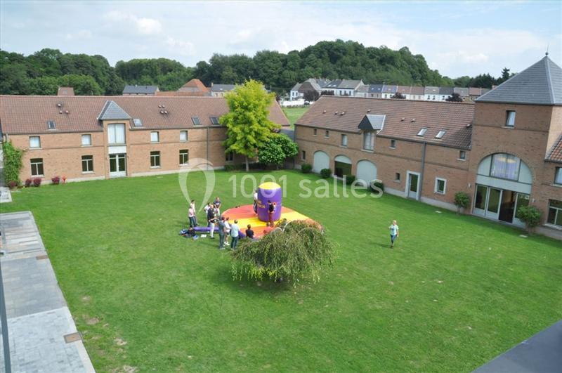 Vue d'une cour verdoyante entourée de bâtiments en briques, avec des personnes autour d'une structure gonflable colorée.