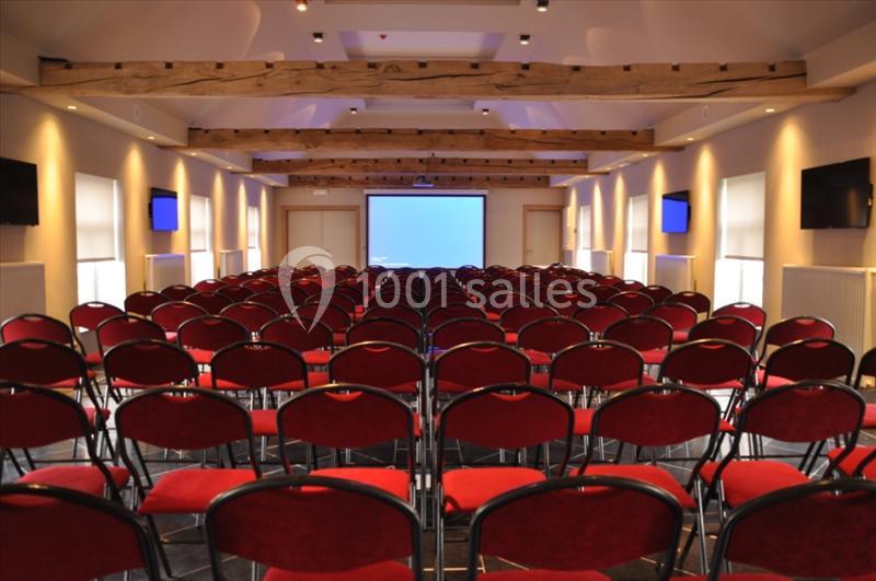 Salle de conférence avec rangées de chaises rouges alignées face à un écran de projection blanc.