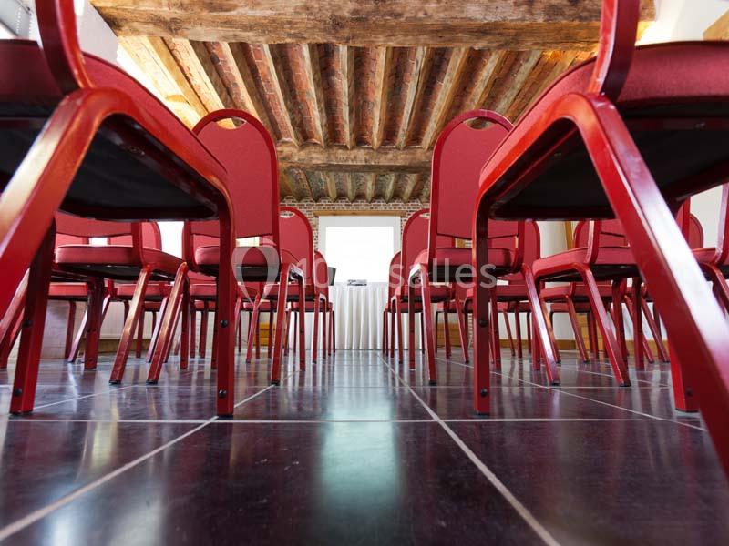Chaises rouges alignées sur un sol en carrelage noir, sous un plafond en poutres de bois apparentes.