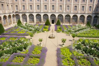 Chambre avec lit double, chevets éclairés, fauteuil, porte-bagages et grande fenêtre avec rideaux translucides.