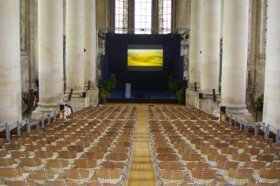 Chambre avec lit double, chevets éclairés, fauteuil, porte-bagages et grande fenêtre avec rideaux translucides.