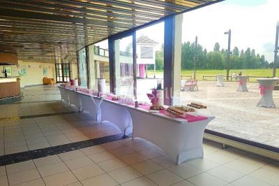 Salle de réception décorée avec des tables rondes, nappes blanches et chaises ornées de nœuds colorés.