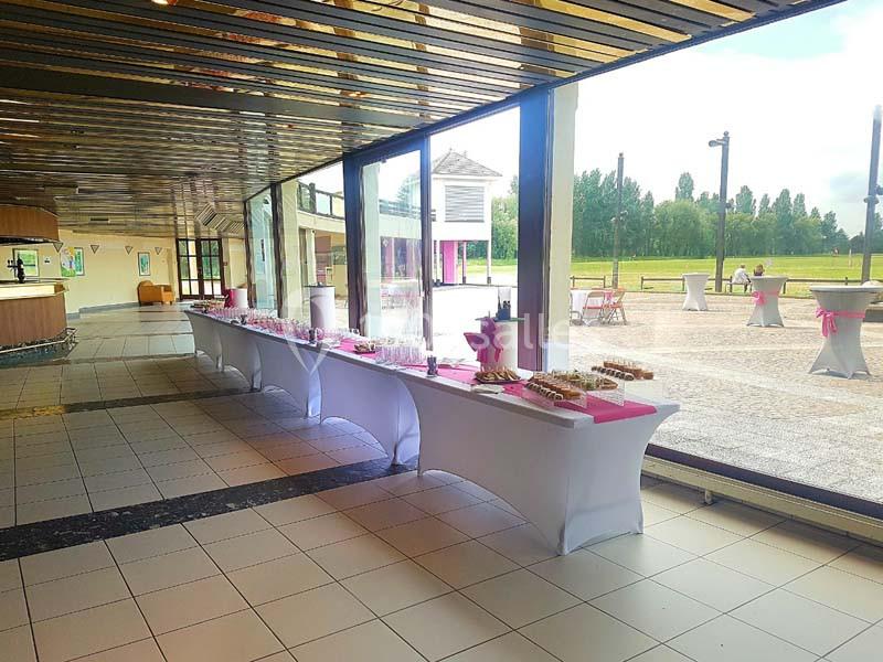 Tables de buffet dressées avec nappes blanches et décorations roses dans une salle lumineuse avec vue sur l'extérieur.