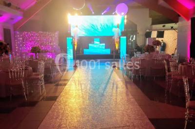 Salle de réception décorée avec des tables rondes, nappes blanches et chaises ornées de nœuds colorés.