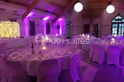 Salle de réception décorée avec des tables rondes, nappes blanches et chaises ornées de nœuds colorés.